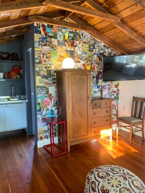 A room with a wooden ceiling, a television, a cabinet, a chair, and a wall covered with colorful images.
