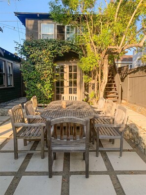 A wooden outdoor dining table with chairs, surrounded by a paved patio.