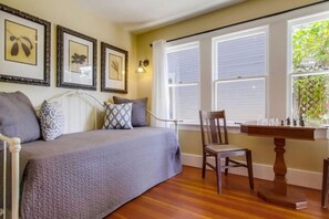 A bedroom with a bed, a chair, a table with chess pieces, and framed pictures on the wall.