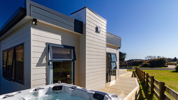 Un bâtiment moderne doté d’un jacuzzi sur une terrasse en bois, de grandes fenêtres et d’une vue sur un parc.