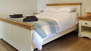 Cama bem arrumada com edredom branco e manta listrada, cabeceira de madeira e mesa de cabeceira com abajur.