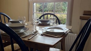 Mesa posta com pratos, tigelas, copos de vinho e talheres, localizada perto de uma janela com vista para o verde.