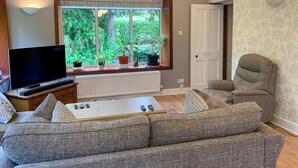 A living room with a large window, a sofa, a chair, a television, and a radiator.