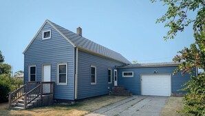 Een blauw huis met twee verdiepingen, een veranda, een garage en een heldere lucht.