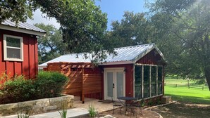 A red wooden building with a covered porch and a small glass enclosure. - Salado Cottage Retreat near Downtown (Salado)