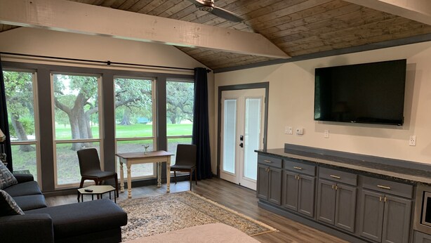 A spacious living area with a large window, a flat-screen TV mounted on the wall, and a cozy seating arrangement. - Salado Cottage Retreat near Downtown (Salado)