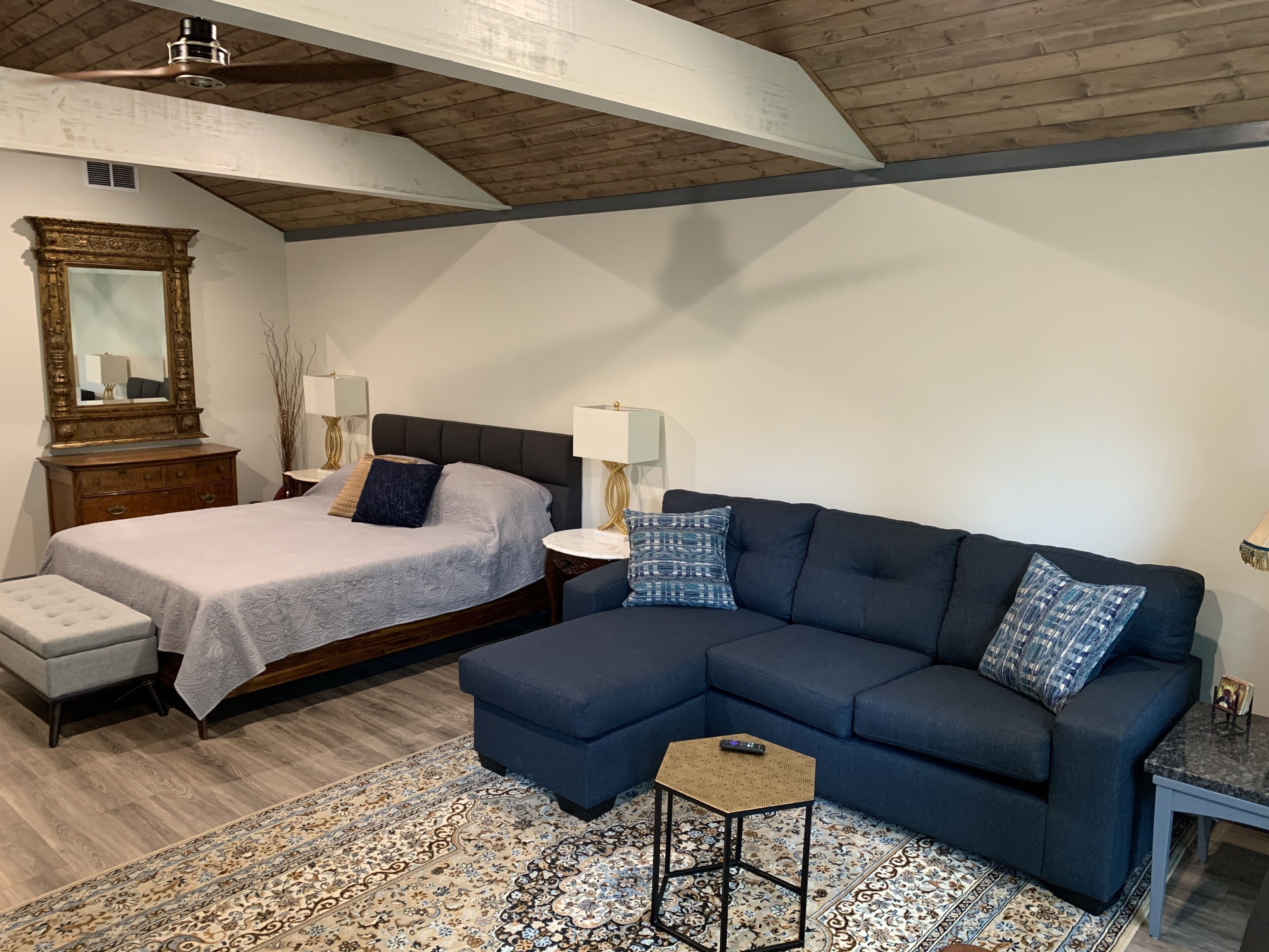 A bedroom with a bed, a sofa, a nightstand, a mirror, and a dresser.