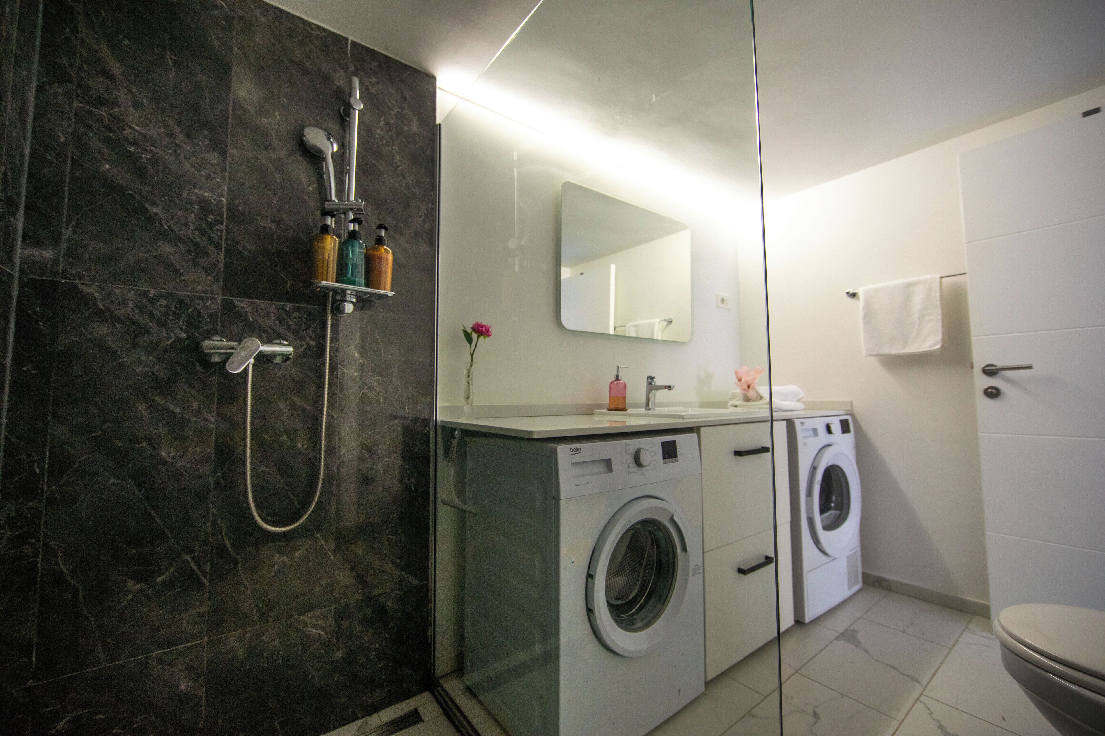 Un baño moderno con cabina de ducha de vidrio, lavadora integrada y un inodoro.