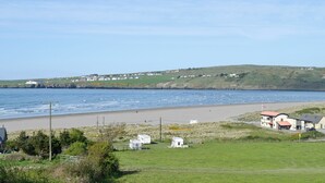 A coastal landscape with a beach, grassy areas, and a few buildings in the distance.