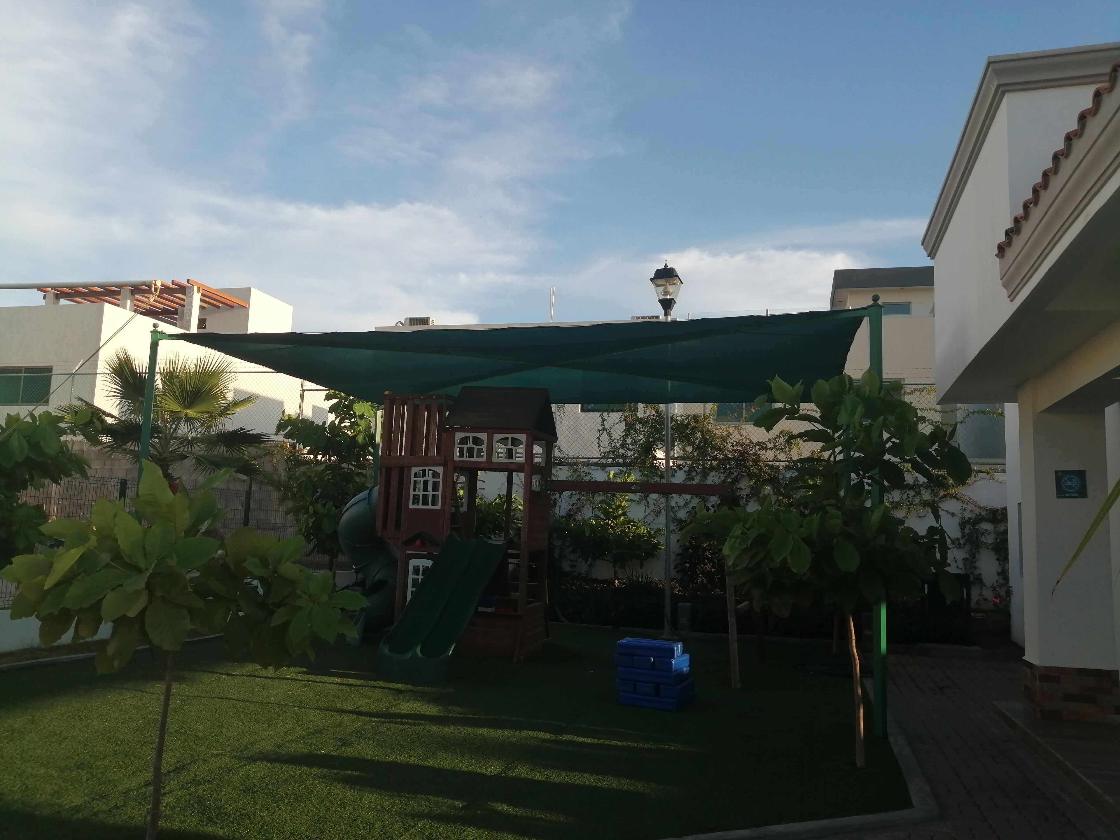 Patio con césped artificial, un parque infantil y un toldo verde.