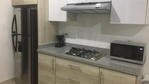 Una cuina amb nevera d'acer inoxidable, fogó de gas, cafetera i microones.