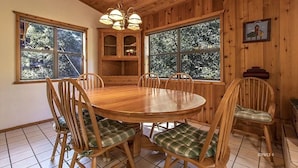 A wooden dining room with a round table and chairs, large windows, and a chandelier. - Treetop Getaway in the Ponderosa Pines (Idyllwild-Pine Cove)