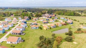 Un quartier résidentiel où les maisons sont disposées selon un plan en damier, entouré de champs verdoyants et d’un étang.
