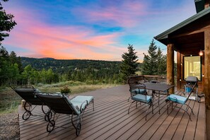 A wooden deck with outdoor furniture, a grill, and a scenic view of a forested mountain range.