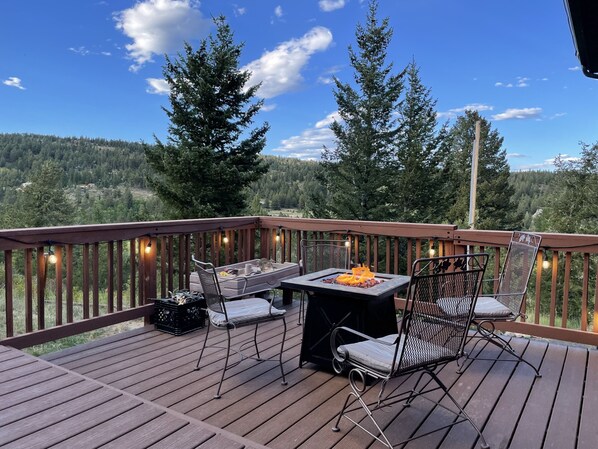 A wooden deck with a table and chairs, overlooking a forested area.