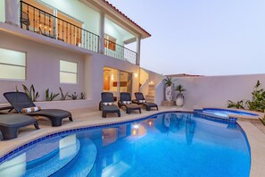 Una piscina con sillones de descanso y un edificio de dos pisos con balcones.