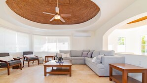 Un salón espacioso con un ventilador de techo grande, un sofá modular gris y muebles de madera.