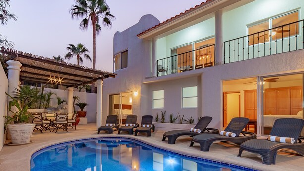 Edificio de dos pisos con piscina, sillas de descanso y un patio cubierto.