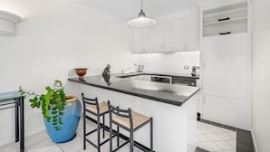 Una cocina moderna con armarios blancos, encimera negra, un jarrón azul grande y tres taburetes de bar.