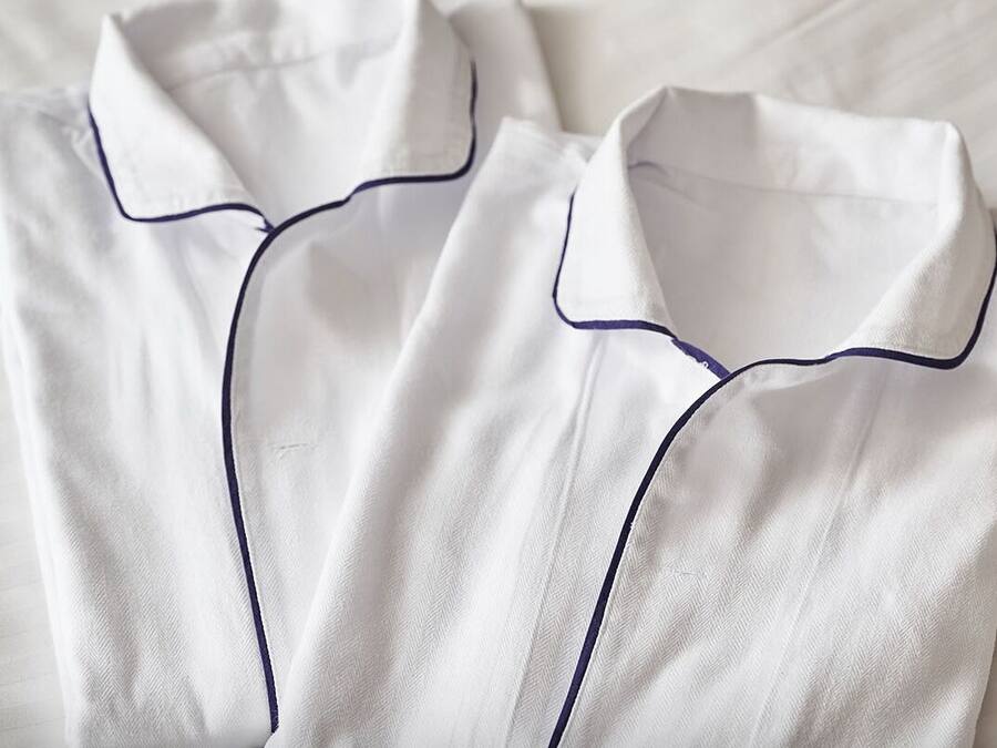 Two neatly folded white shirts with dark blue piping.