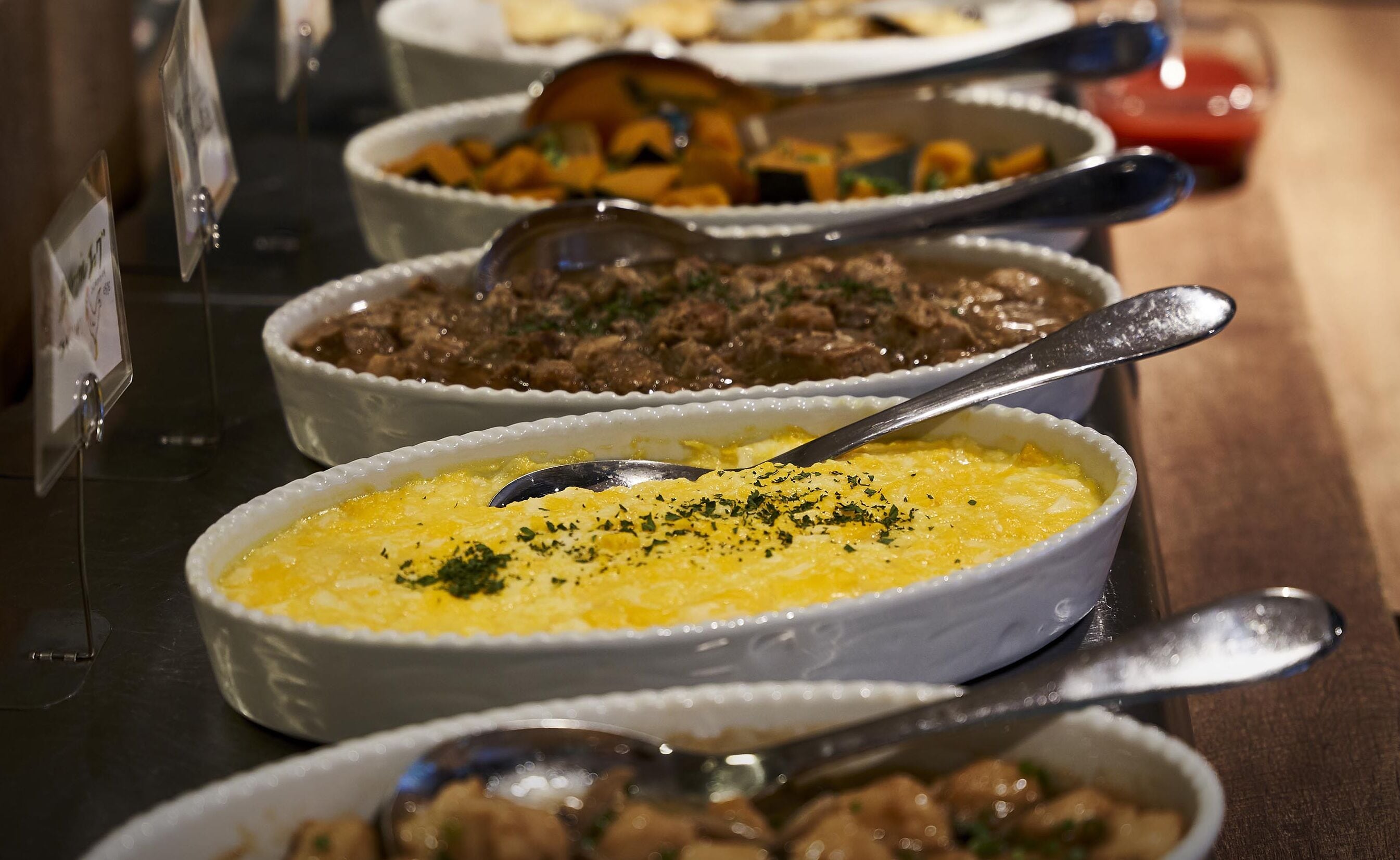 Buffet com diversos pratos em tigelas brancas, incluindo um prato de arroz amarelo com ervas.