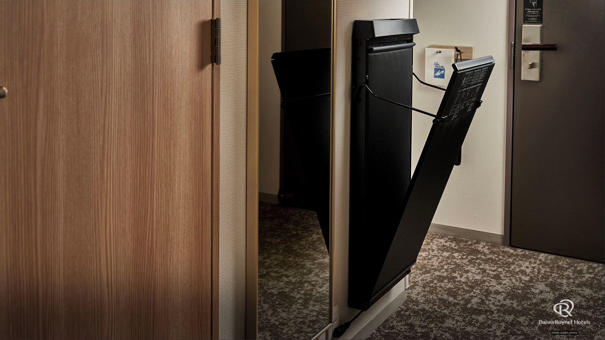 Ein Hotelzimmer mit einer Holztür, einem schwarzen Schrank und einem kleinen Schreibtisch mit einem Computer.