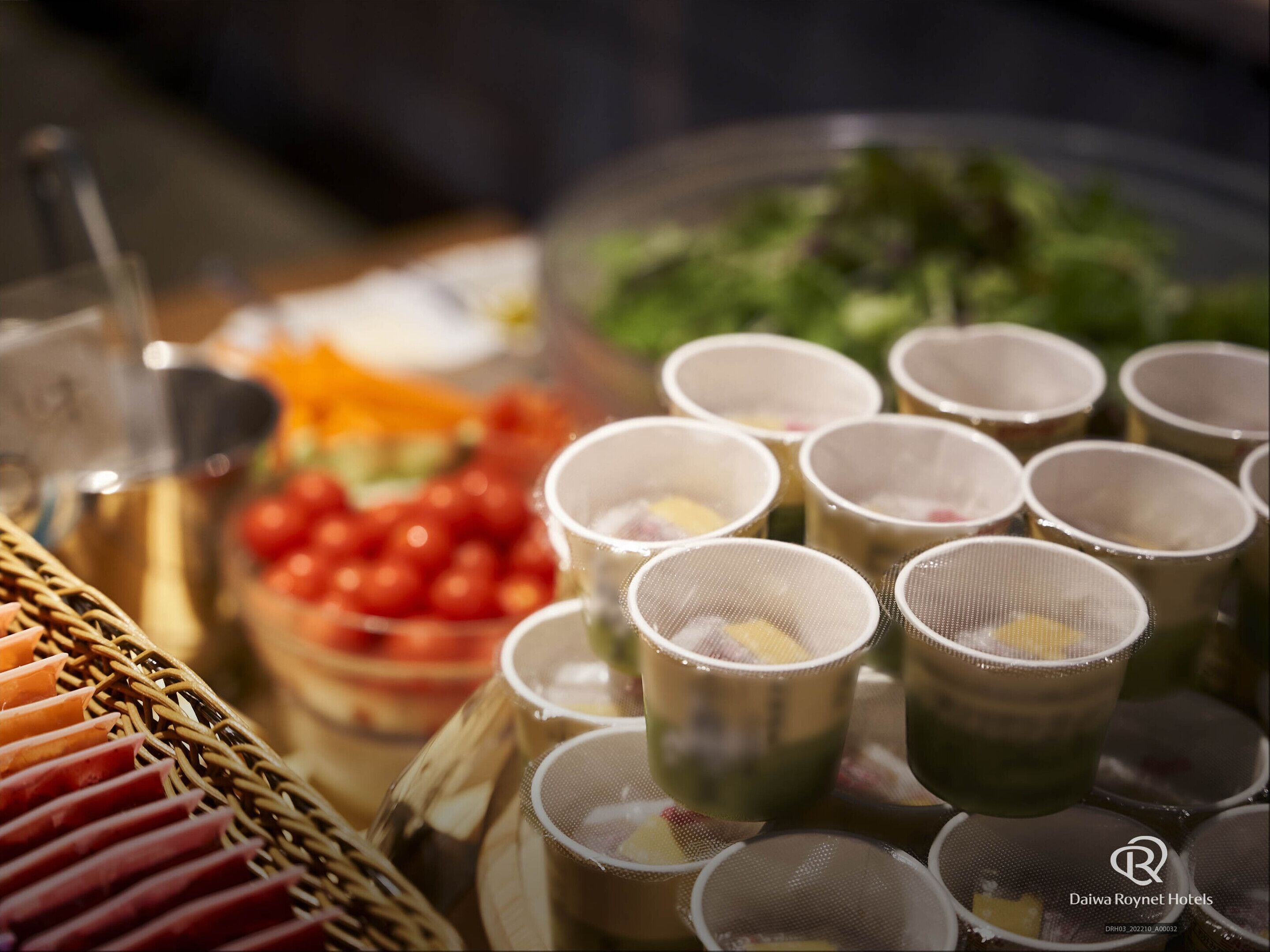 Uma mesa de buffet com diversos alimentos e pequenos copos com tampas de coador.