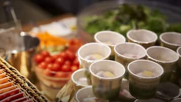 Uma mesa de buffet com diversos alimentos e pequenos copos com tampas de coador.