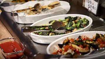 A buffet with various dishes, including vegetables and a bowl of sauce.
