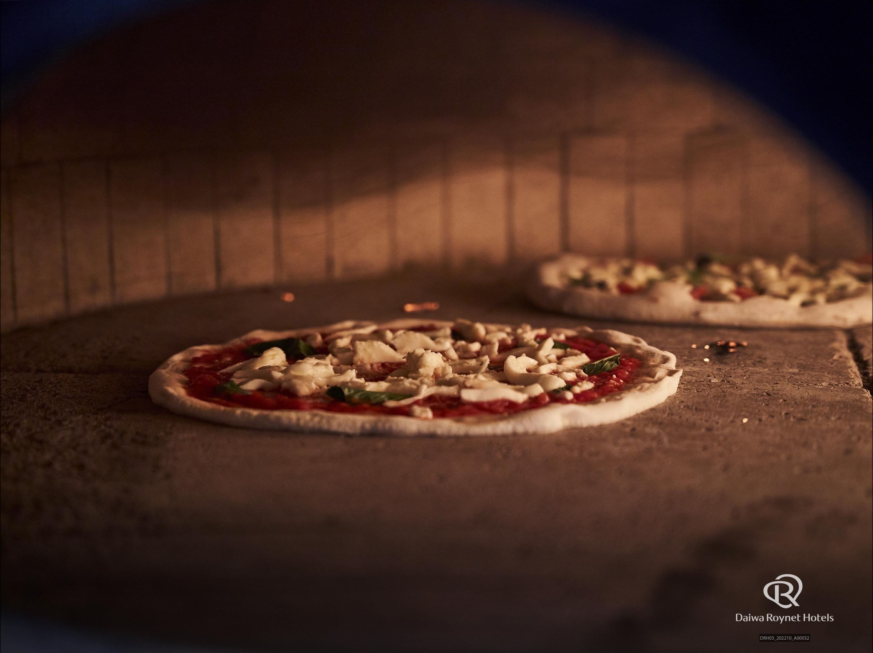 Kaksi pizzaa puupinnalla tiiliuunin sisällä.