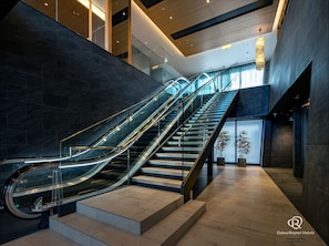 A modern hotel lobby with a glass elevator, a staircase, and a potted plant. - Daiwa Roynet Hotel Kanazawa-eki Nishiguchi (Kanazawa)
