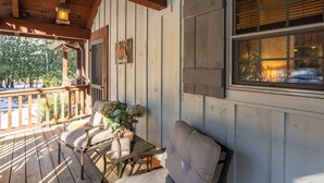 Una terraza de madera con mobiliario exterior, un letrero de bienvenida y una ventana con persianas.