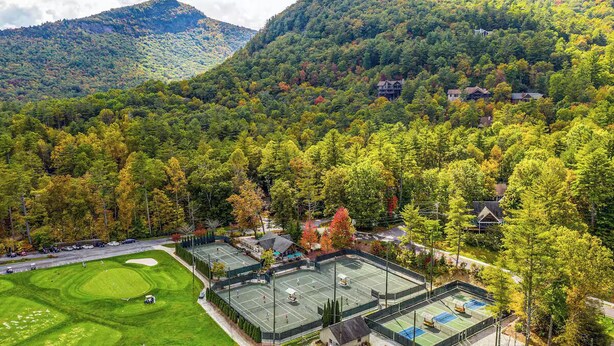 Un campo de golf con varias canchas, rodeado por un área boscosa con casas al fondo.