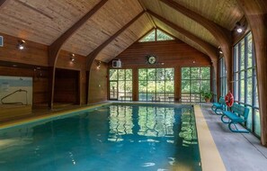 Una piscina interior con vigas de madera, ventanas amplias y bancos a lo largo de la pared.