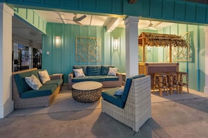 A covered outdoor seating area with wicker furniture, a round coffee table, and a thatched roof structure. - Stunning views at this large oceanfront home w/pool and game room ready for family fun! (North Myrtle Beach)