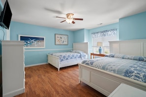 A bedroom with two beds, a ceiling fan, and artwork on the walls.