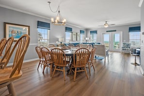 A spacious dining area with a round table and wooden chairs, a chandelier, and a view of the ocean through large windows. - Stunning views at this large oceanfront home w/pool and game room ready for family fun! (North Myrtle Beach)