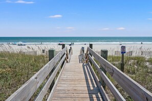 Ein Holzsteig führt zu einem Strand, an dem ein Schild darauf hinweist, die Dünen zu schonen.