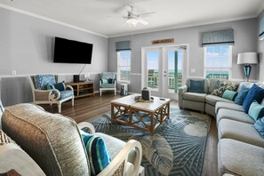 Ein Wohnzimmer mit Flachbildfernseher, Deckenventilator, großem Fenster und Holz-Couchtisch.