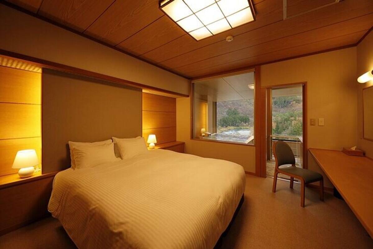 A hotel room with a large bed, bedside lamps, a desk, and a window with a view of a mountainous landscape.
