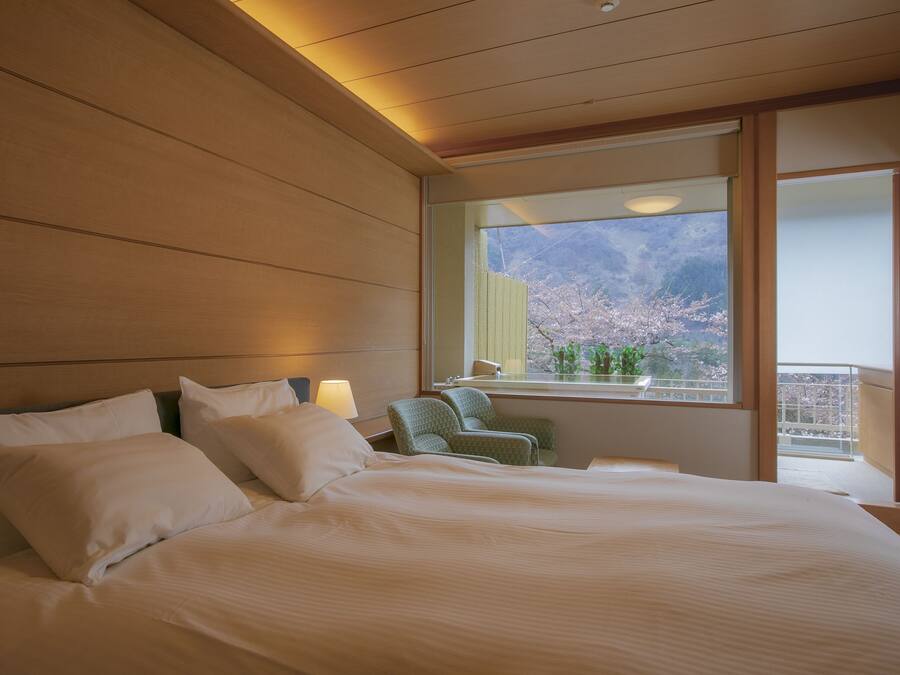 Ein Hotelzimmer mit einem großen Bett, einem Sessel, einem Fenster mit Bergblick und einem Balkon.