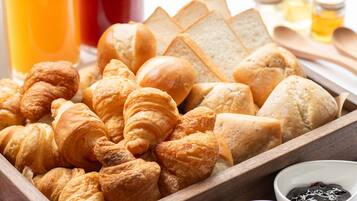 A wooden tray filled with various types of bread and pastries, including croissants and baguettes, accompanied by a small bowl of jam.