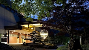 Un edificio moderno con un jardín tradicional japonés, que incluye un estanque con carpas koi, faroles y un árbol grande.