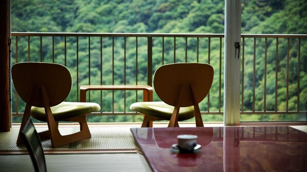 Una habitación con dos sillas de madera y una pequeña mesa, con vista a un bosque a través de la barandilla de un balcón.