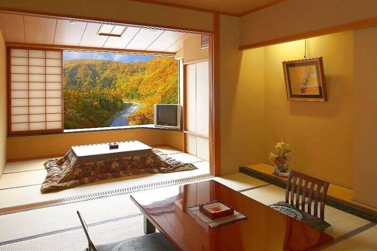 A tatami mat room with a view of a forest and a river, a traditional Japanese TV, and a small table with a red book.