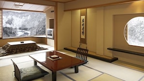 Una habitación japonesa tradicional con suelo de tatami, una mesa baja, un banco acolchado y un ventanal con vistas nevadas.