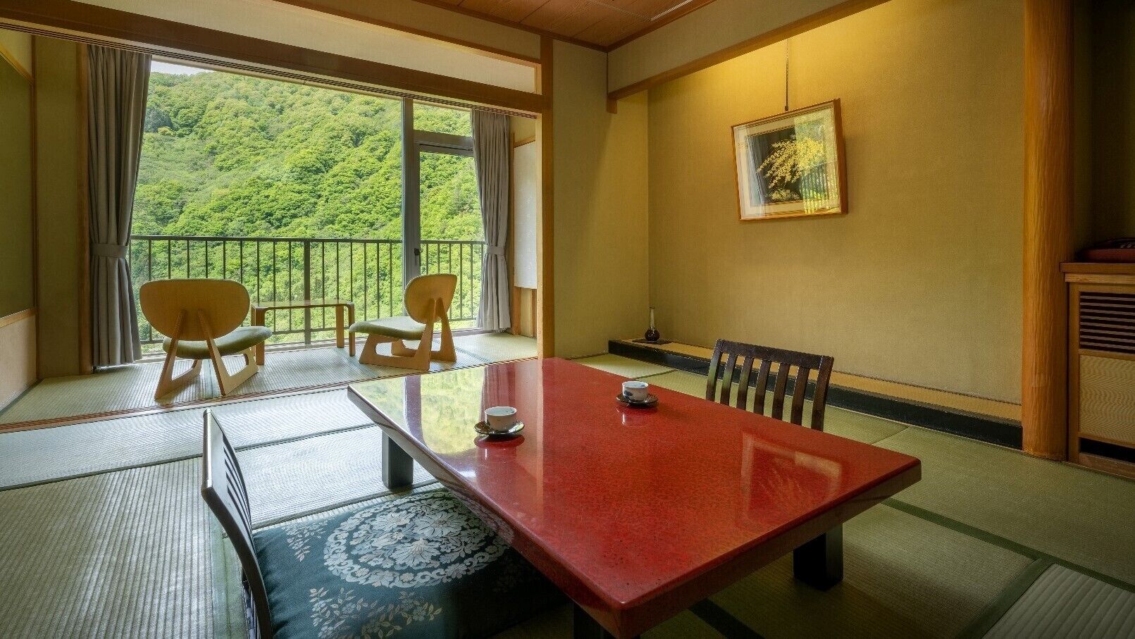 A traditional Japanese-style room with tatami flooring, a low table with a cup, and a view of a forested area.