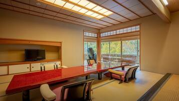 A traditional Japanese-style room with tatami flooring, a low table with a red runner, and a television on a wooden shelf.