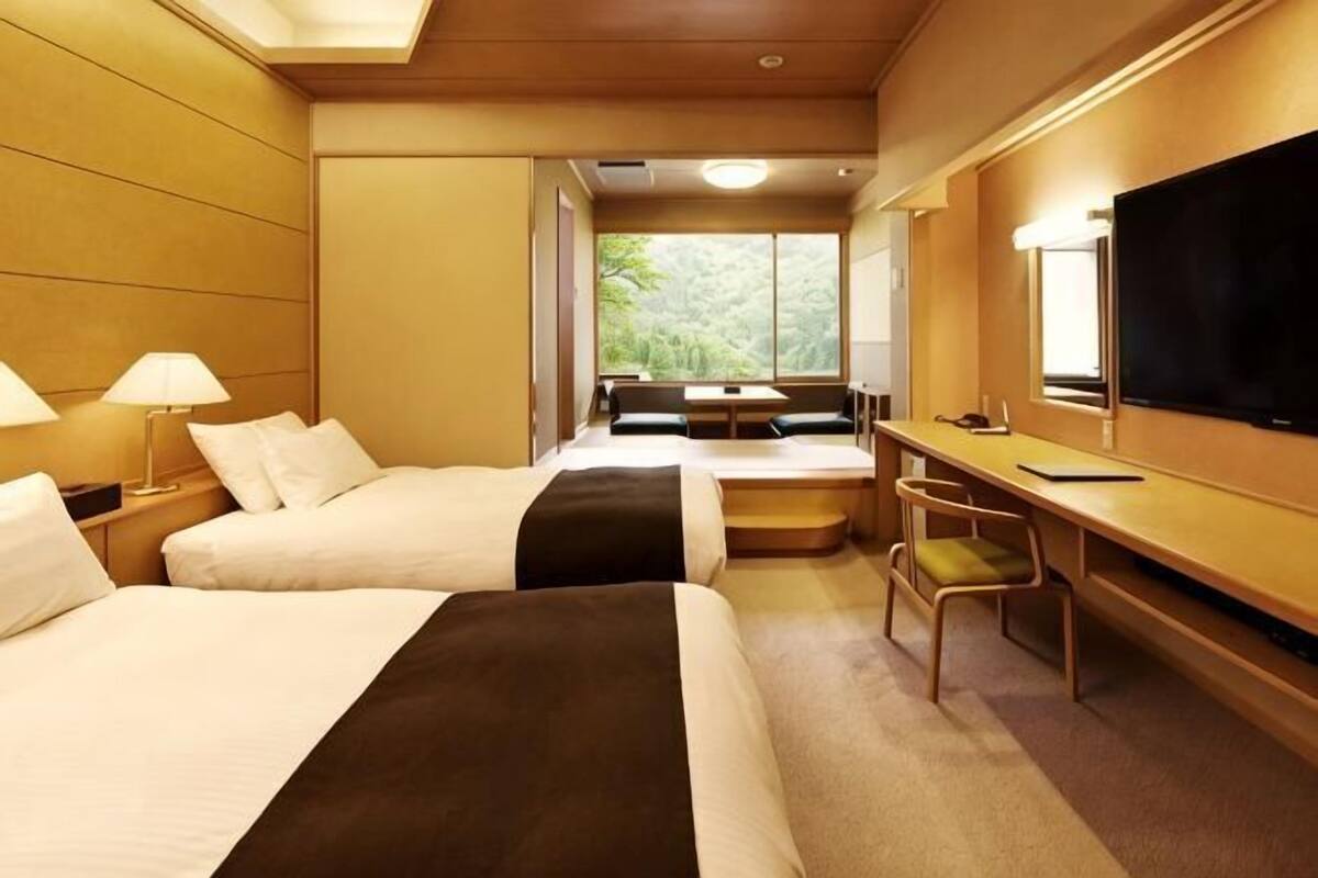A hotel room with two beds, a desk, a chair, a TV, and a window with a view.