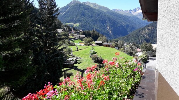 A balcony with a view of a mountain village, potted flowers, and a clear sky. - Apartment with garden in prime location (Tobadill)